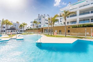 Een zwembadterras met een heldere lucht, palmbomen en moderne gebouwen op de achtergrond.