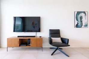 Una sala de estar moderna con televisor de pantalla plana, mueble de entretenimiento de madera, una silla de oficina negra y arte abstracto en la pared.