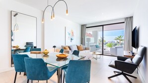 A modern living room with a glass dining table, blue chairs, a black leather sofa, and a TV mounted on the wall. - Santa Barbara Heights IV CLC - Luxury, private plunge pool (Mijas Costa)