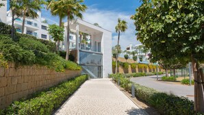 A modern building with a paved walkway, surrounded by greenery and palm trees. - Santa Barbara Heights IV CLC - Luxury, private plunge pool (Mijas Costa)