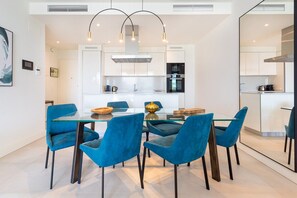 Una cocina moderna con armarios blancos, una isla central y sillas azules alrededor de una mesa de vidrio.