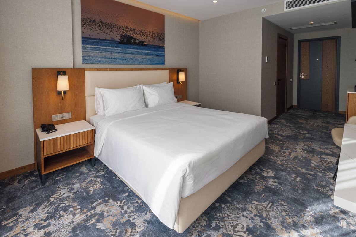 Une chambre d’hôtel avec un grand lit, deux tables de chevet avec des lampes, un tableau au mur et une moquette à motifs.
