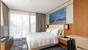 Ein Hotelzimmer mit einem großen Bett, einem Schreibtisch, einem Sessel, einem Fernseher und einem Gemälde an der Wand.