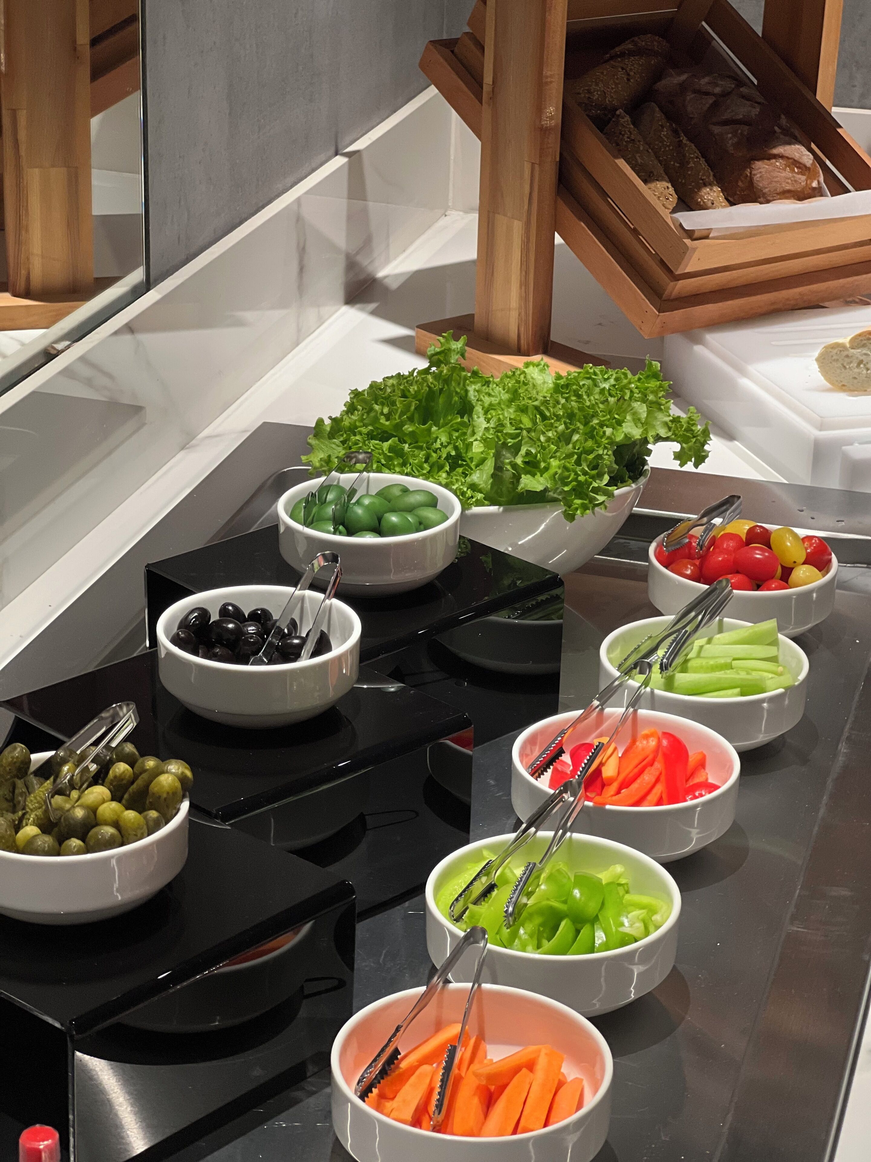 Buffet com diversos alimentos, incluindo azeitonas, azeitonas verdes, tomates cereja, cenouras, aipo e alface.