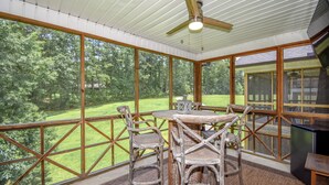 Un área de comedor al aire libre techada, con una mesa, sillas, un ventilador de techo y vistas a un paisaje verde.