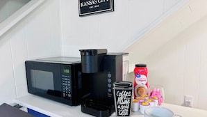 Un piano di lavoro in cucina con un forno a microonde, una macchina da caffè e tazze da caffè. Un cartello sopra recita 'Kansas City'.