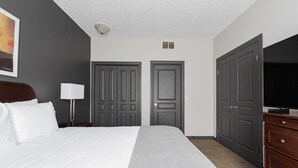 Ein Hotelzimmer mit einem großen Bett, zwei Schränken, einem Fernseher und einem Gemälde an der Wand.