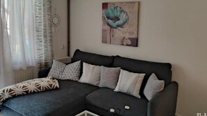 A modern living room with a dark grey sectional sofa, patterned cushions, and a wall-mounted abstract painting.