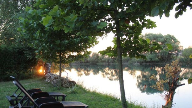 A serene lakeside setting with a picnic table and chairs under a tree, surrounded by lush greenery. - Four bedroom house with river view (Bihac)