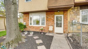 A two-story building with a brick facade, a front door, and a small porch area with potted plants and a chair. - Walk to Mall & Train Station! Philly Suburb Stay (Willow Grove)