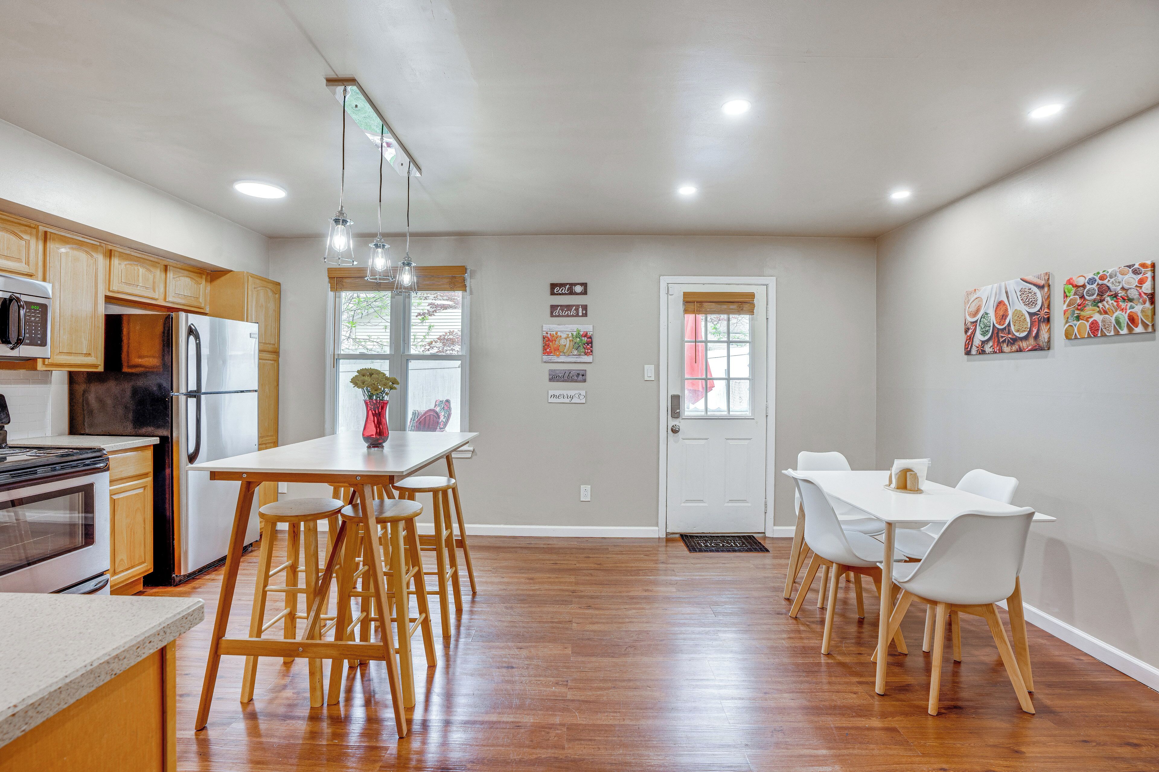 Une cuisine moderne avec des meubles en bois, un réfrigérateur en acier inoxydable et un coin repas comprenant une table et des chaises blanches.