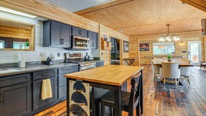 A modern kitchen with dark cabinets, a wooden island, and a dining area with a large table and chairs. - Fire Pit + Sauna: Inviting Utah Cabin (Duck Creek Village)