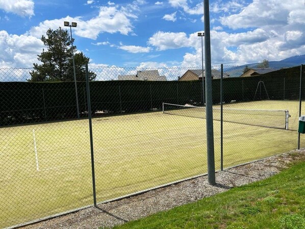 A tennis court enclosed by a chain-link fence with a net in the center, surrounded by a grassy area and a building in the background. - Apartment 2 rooms Pool, Terrace, Views, 6 Pax & Wi-Fi (Bourg-Madame)