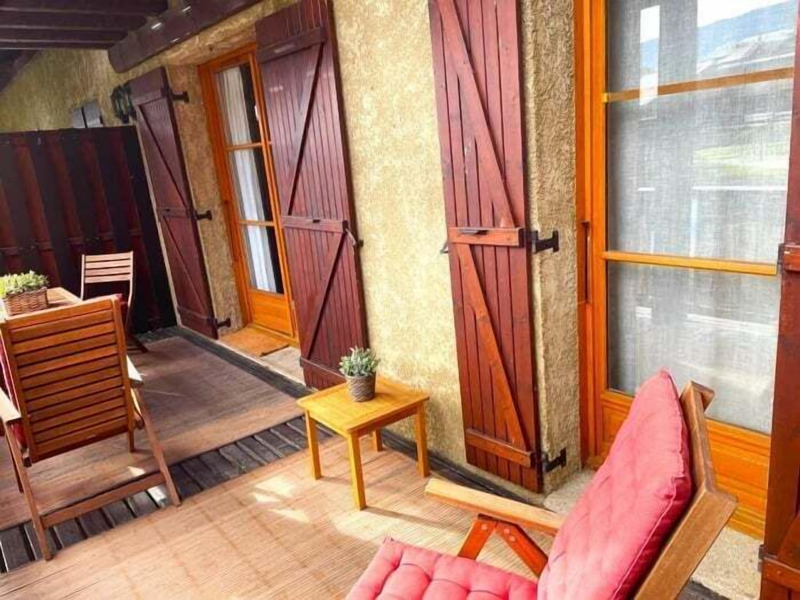 Un espace extérieur accueillant, aménagé avec du mobilier en bois et une chaise rembourrée de couleur rouge.