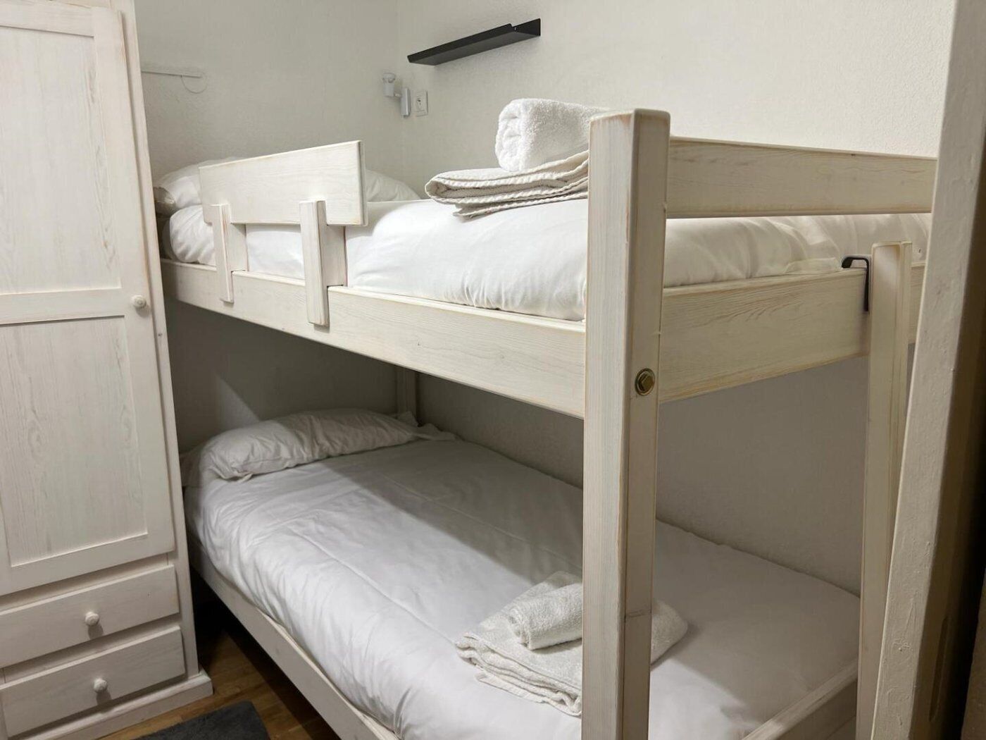 A bunk bed room with white bedding and a towel on the top bunk.