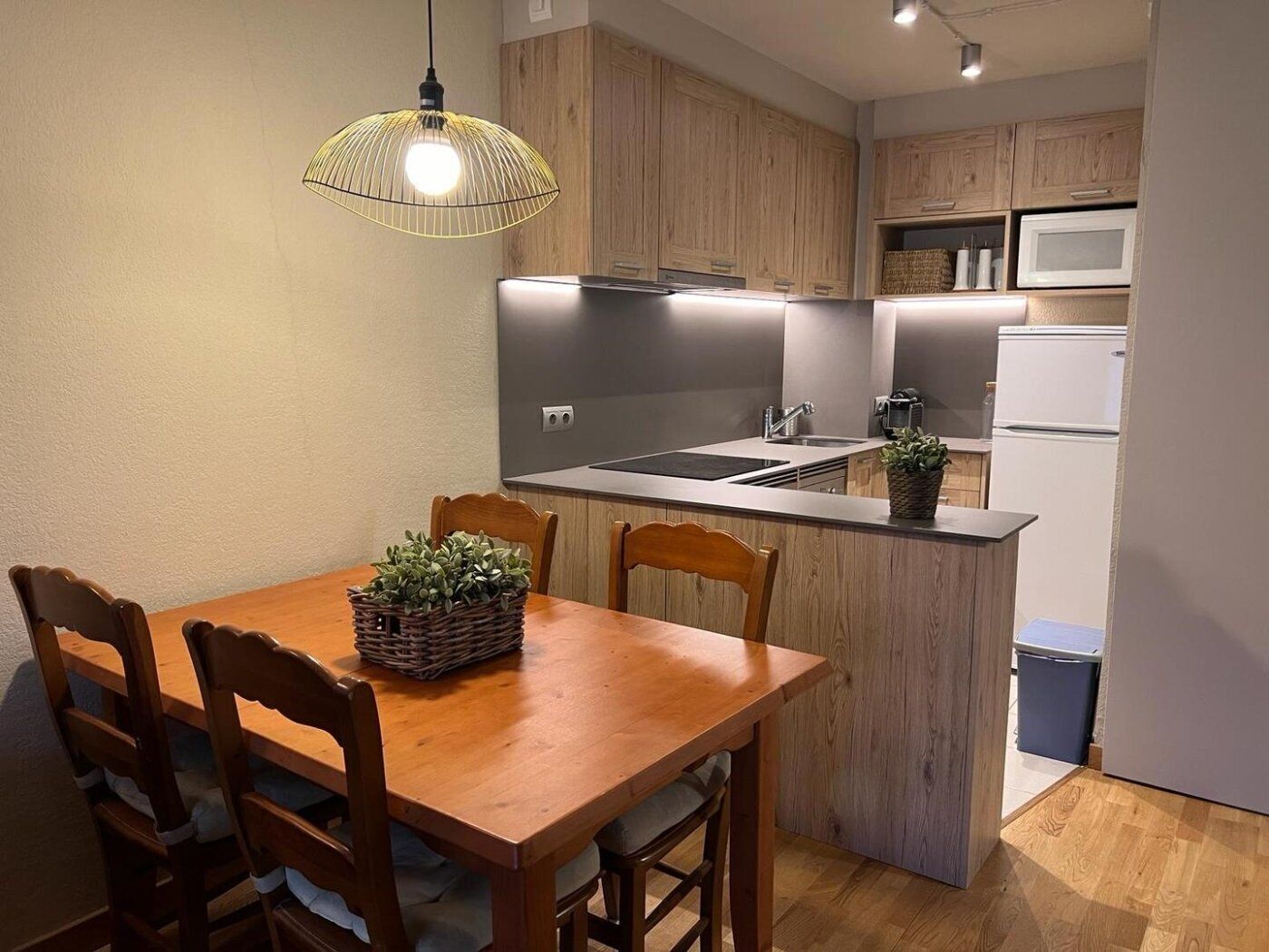 A modern kitchen with wooden cabinets, a built-in microwave, and a dining area with a wooden table and chairs.