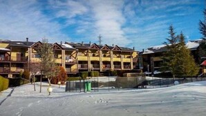Un hôtel à plusieurs étages doté de balcons, une piste de ski au premier plan et un ciel dégagé.