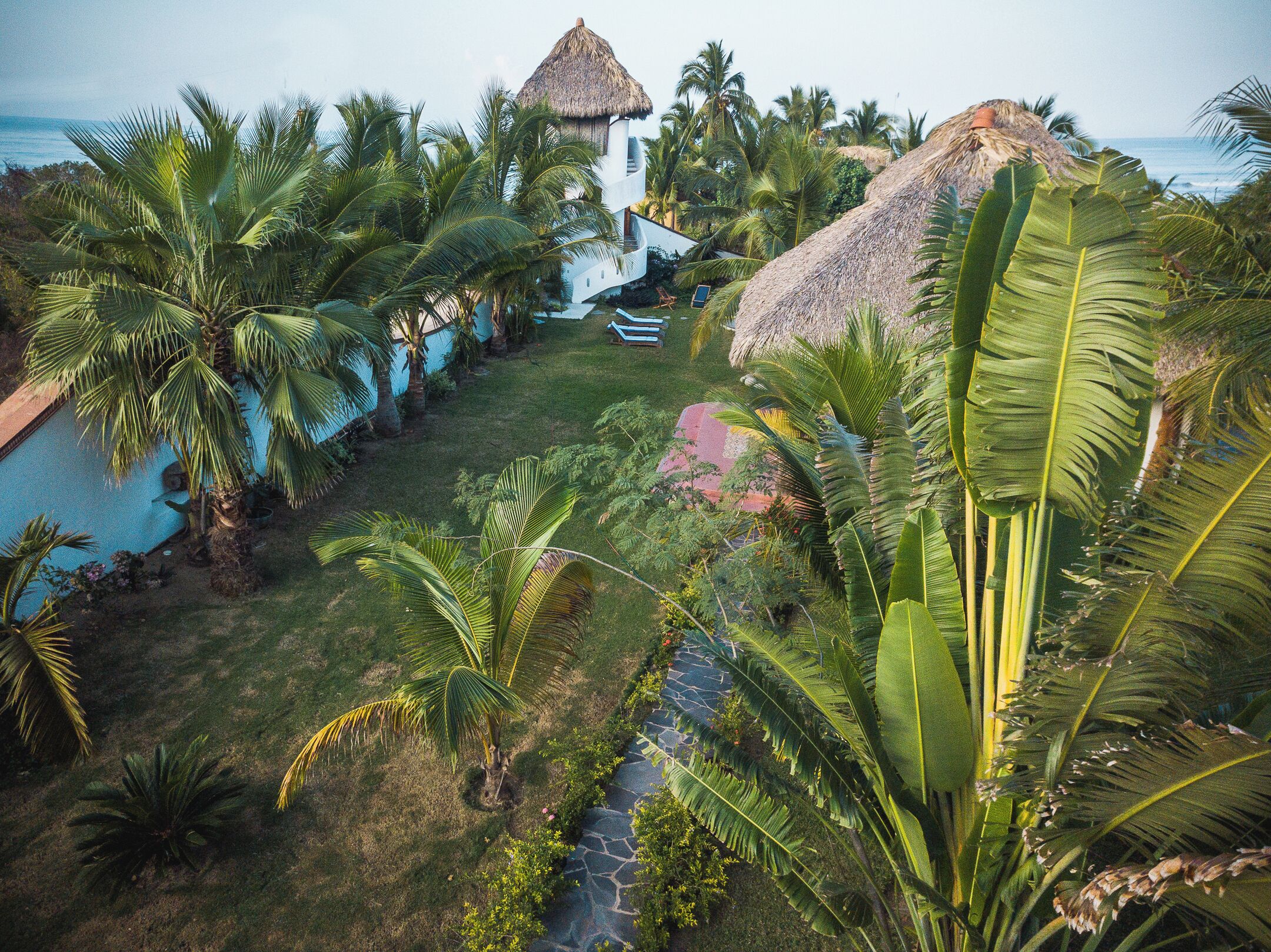 Un resort tropical con un edificio de techo de paja, palmeras y una vista despejada del océano.