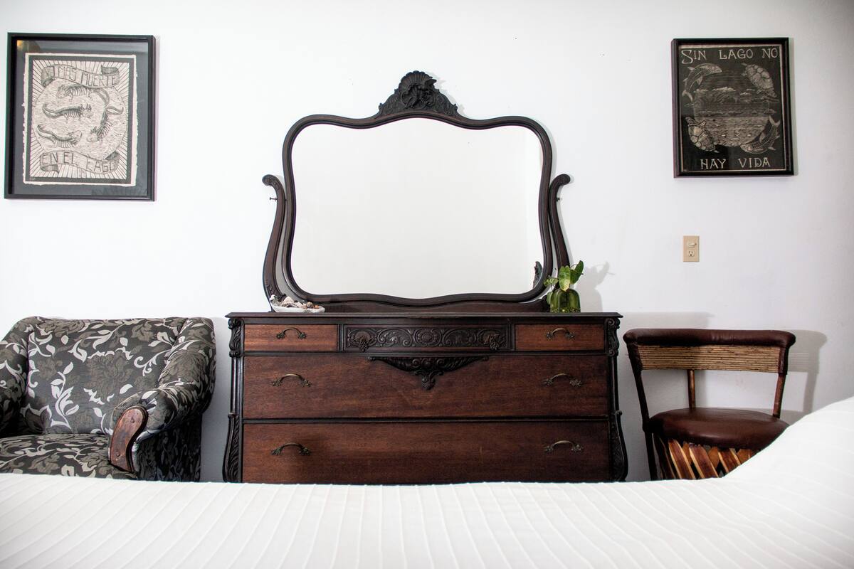 A bedroom with a wooden dresser, a chair, a bed, and two framed pictures on the wall.