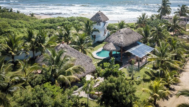 A resort with a pool, thatched-roof structures, and a view of the ocean. - El MURO MAJAHUA RETREAT CENTER (Troncones)