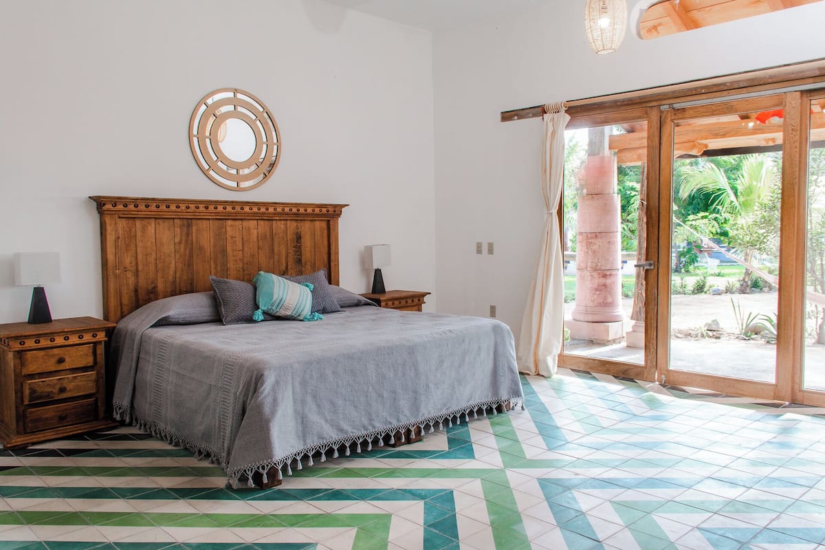 A bedroom with a wooden headboard, a bed with a grey bedspread, two bedside tables with lamps, and a patterned floor.