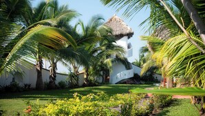 A tropical resort with a thatched-roof building surrounded by lush palm trees and a well-maintained garden. - El MURO MAJAHUA RETREAT CENTER (Troncones)