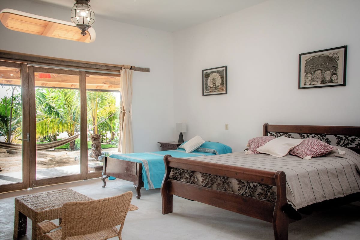 A bedroom with a bed, a chair, a nightstand, and a large window with a view of palm trees.