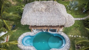 A thatched-roof structure with a circular pool, surrounded by palm trees and a stone pathway. - El MURO MAJAHUA RETREAT CENTER (Troncones)