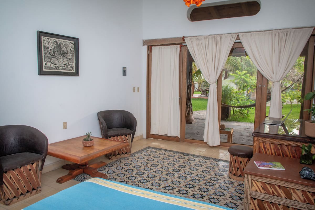 A room with a wooden table, two chairs, a sofa, a patterned rug, and a framed picture on the wall.