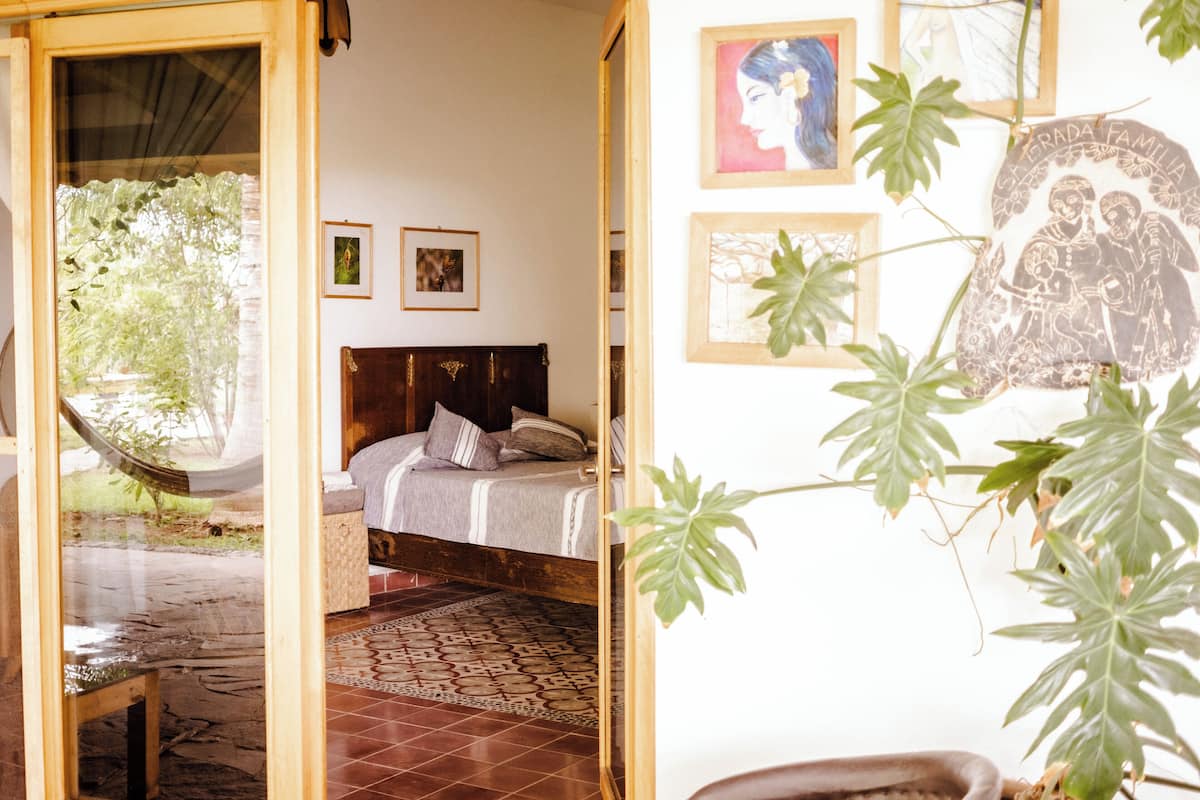 A room with a bed, a hammock, and a view of greenery outside.