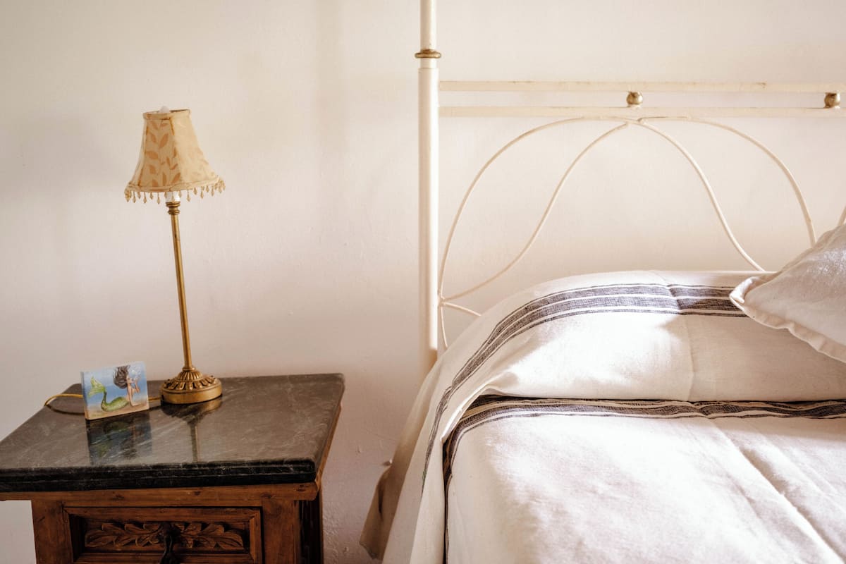 A bed with a metal headboard, a bedside table with a lamp, and a picture frame.