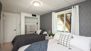 Ein Schlafzimmer mit zwei Betten, einem Schminktisch, einem Fenster mit Vorhängen und einer Treppe, die durch das Fenster sichtbar ist.