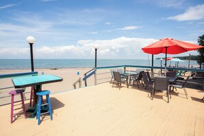 Une terrasse au bord de la plage, avec des tables et des chaises, une piscine et une vue sur l’océan.