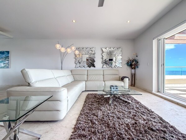 A modern living room with a white sectional sofa, a glass coffee table, and decorative wall art.