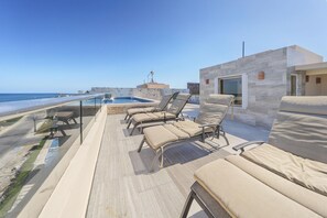 A rooftop pool area with lounge chairs and a view of the ocean.