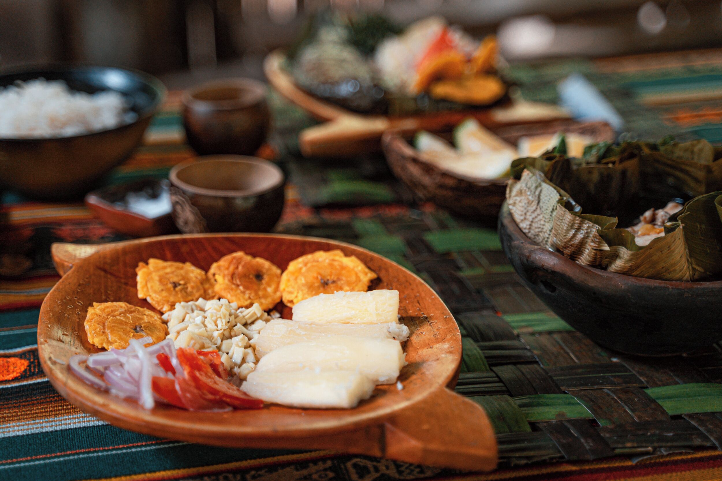 A table with various dishes, including a bowl of rice, a plate with sliced bananas, and a bowl of tamales.