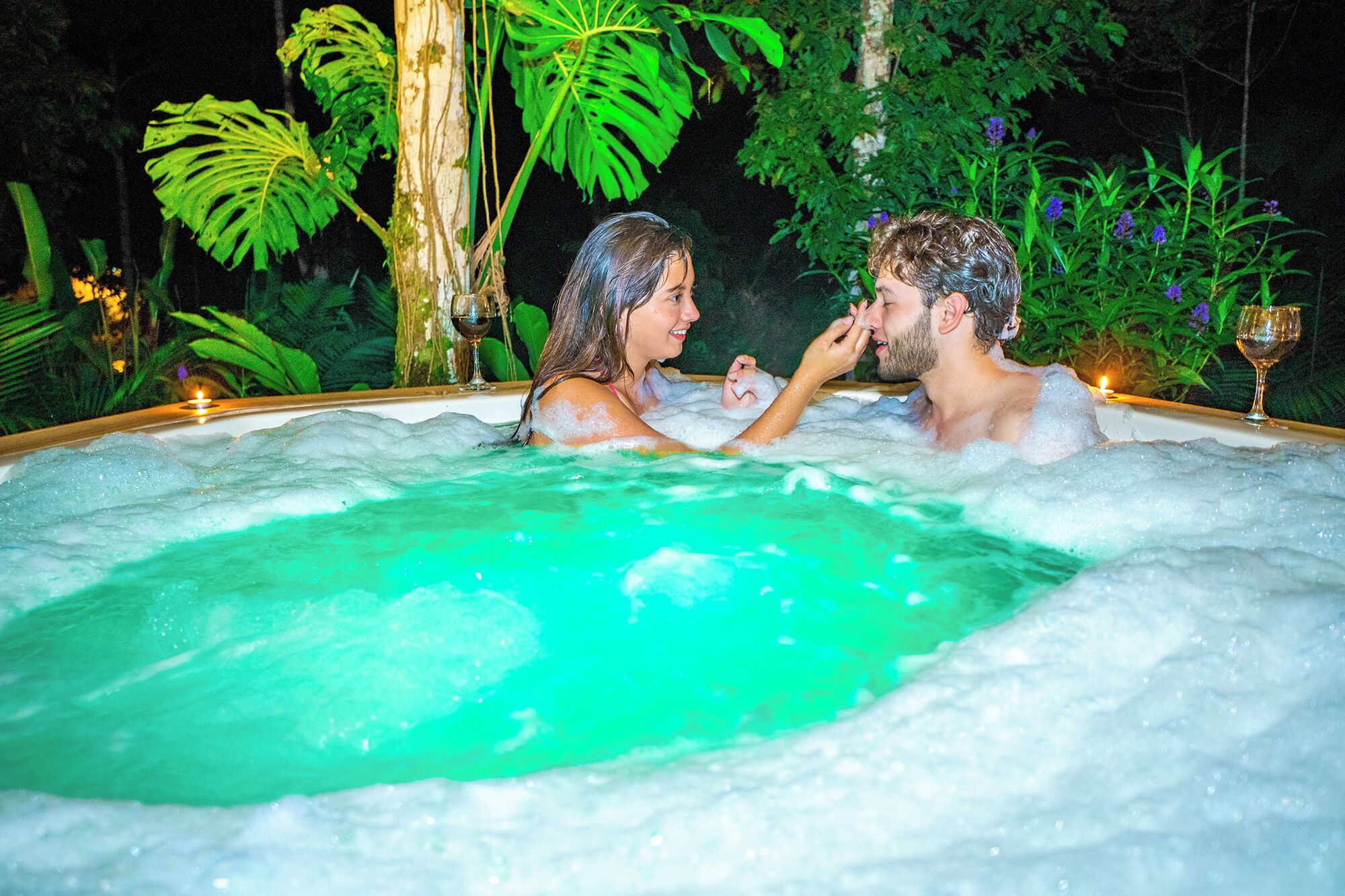 A couple in a hot tub surrounded by lush greenery.