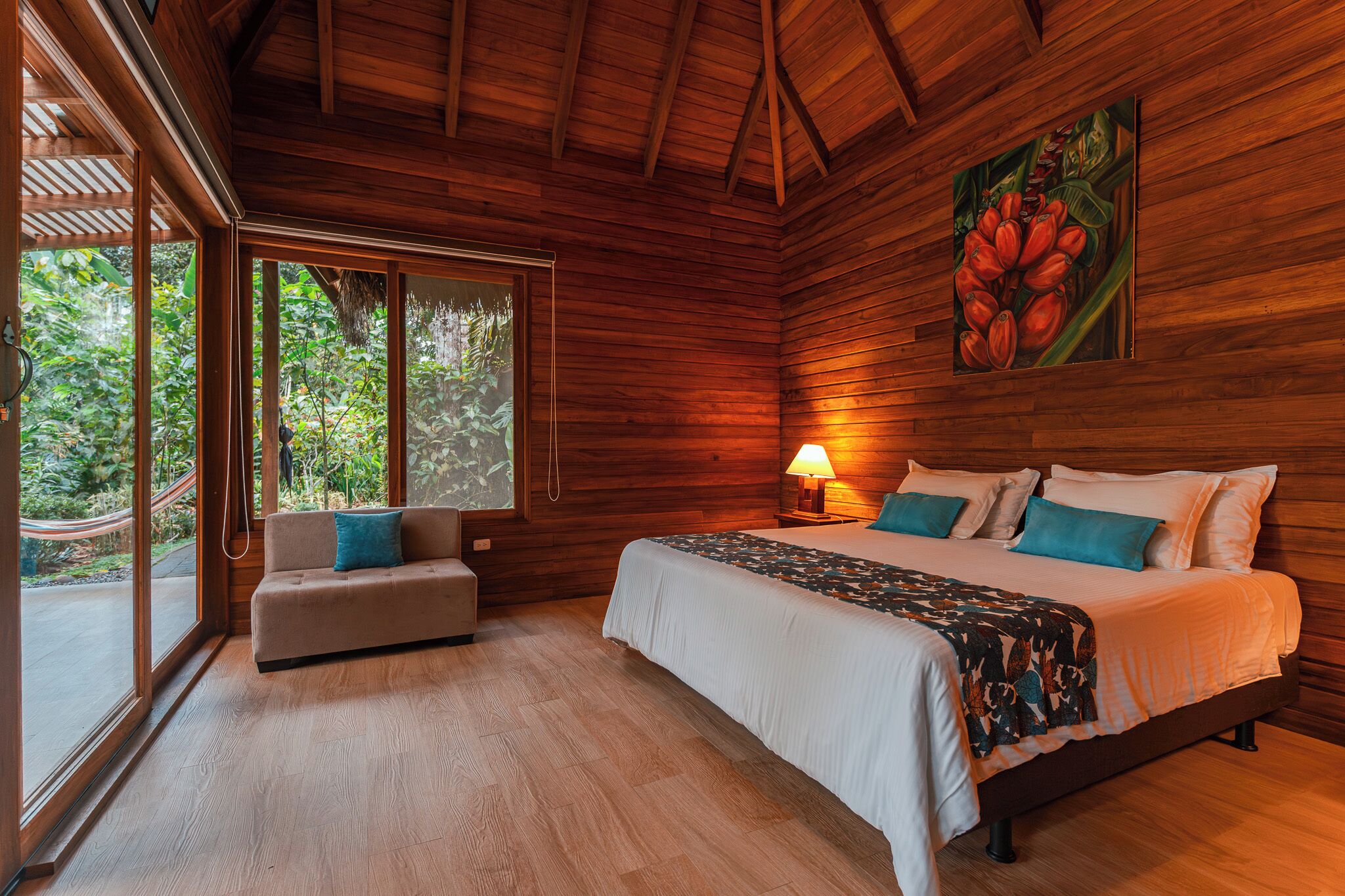 A wooden room with a bed, a sofa, and a window overlooking greenery.