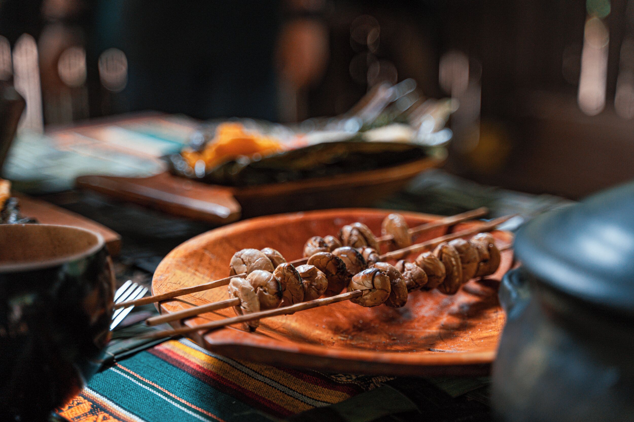 Une table en bois avec des brochettes de nourriture, un bol et une casserole.