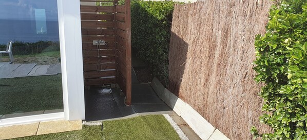 A modern outdoor shower area with a wooden fence, a grassy lawn, and a hedge.