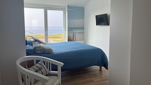 Un dormitorio con una cama grande, una silla blanca y vista al océano.