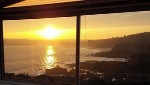 Vista del atardecer desde una habitación con amplias ventanas que dan a un paisaje costero.
