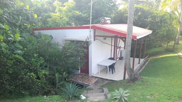 A small, single-story structure with a red roof and white walls, featuring a patio with a table and chairs.
