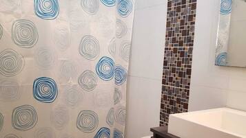 A bathroom with a toilet, a shower curtain with a geometric pattern, a tiled wall, and a sink.