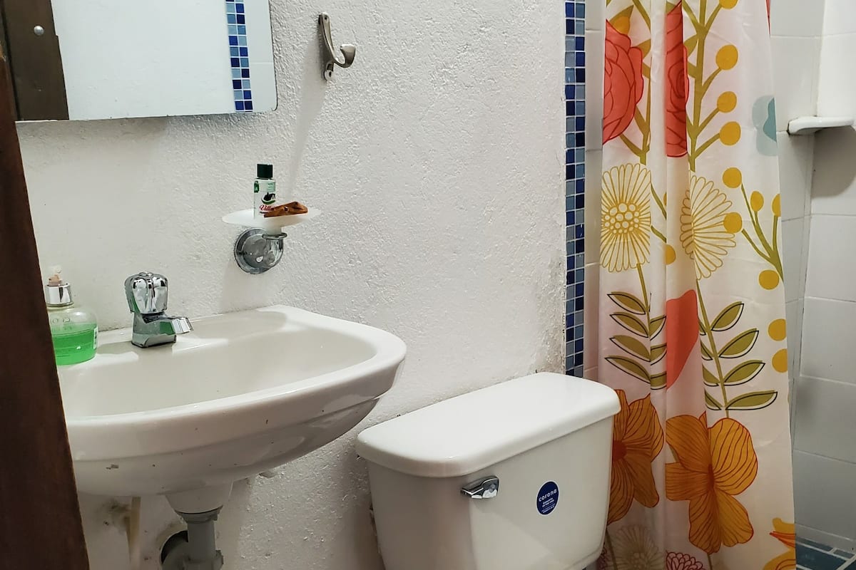 Un baño con un lavamanos, dos inodoros, un cubo de basura y una cortina de ducha con estampado floral.
