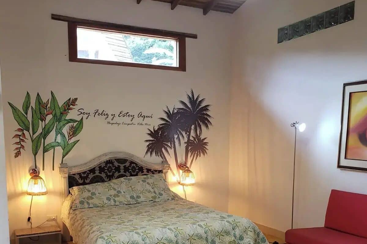 Un dormitorio con una cama, dos lámparas de pared, un sofá rojo y un cuadro enmarcado.