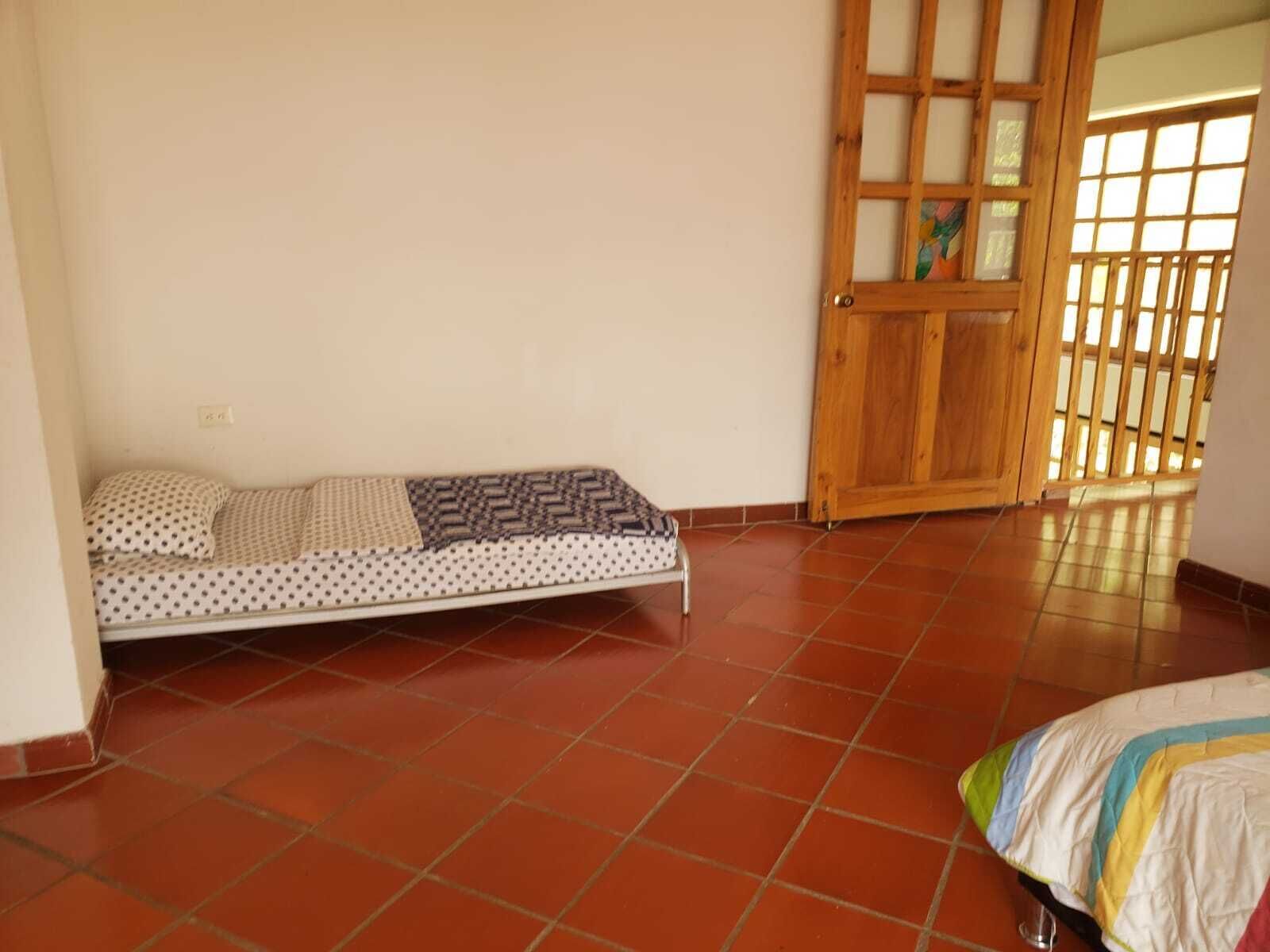 Una cama individual con una colcha estampada, piso de baldosas y una puerta de madera con un ventanal.