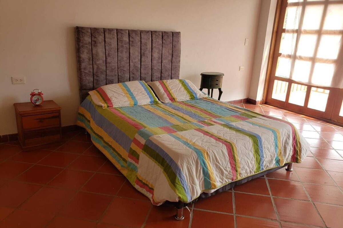 Un dormitorio con cama, mesita de noche, una pequeña mesa y ventana.