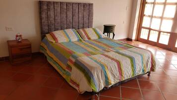 A bedroom with a bed, a nightstand, a small table, and a window.