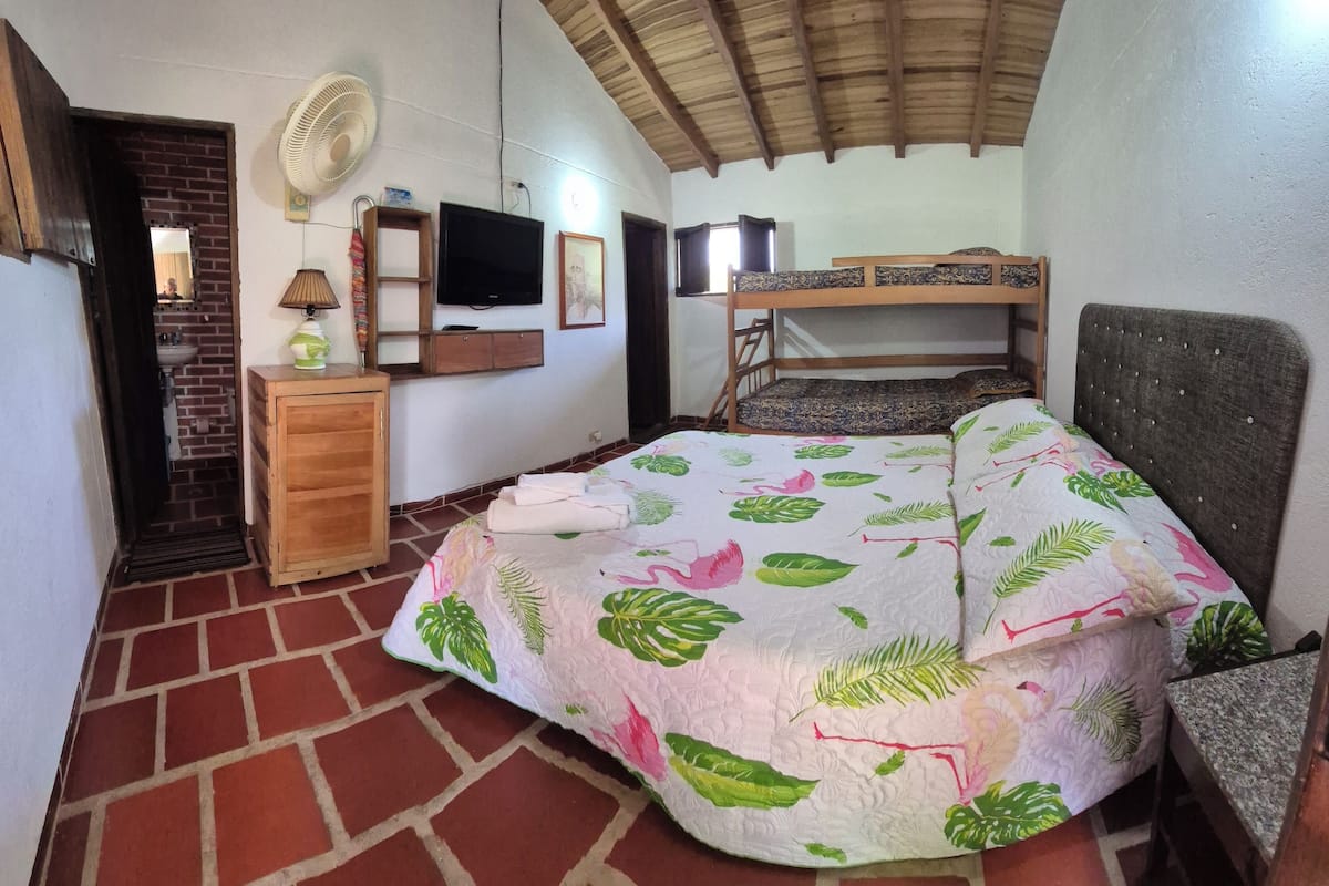 Una habitación con una cama, un armario de madera, un ventilador, un televisor y una pared de ladrillo.